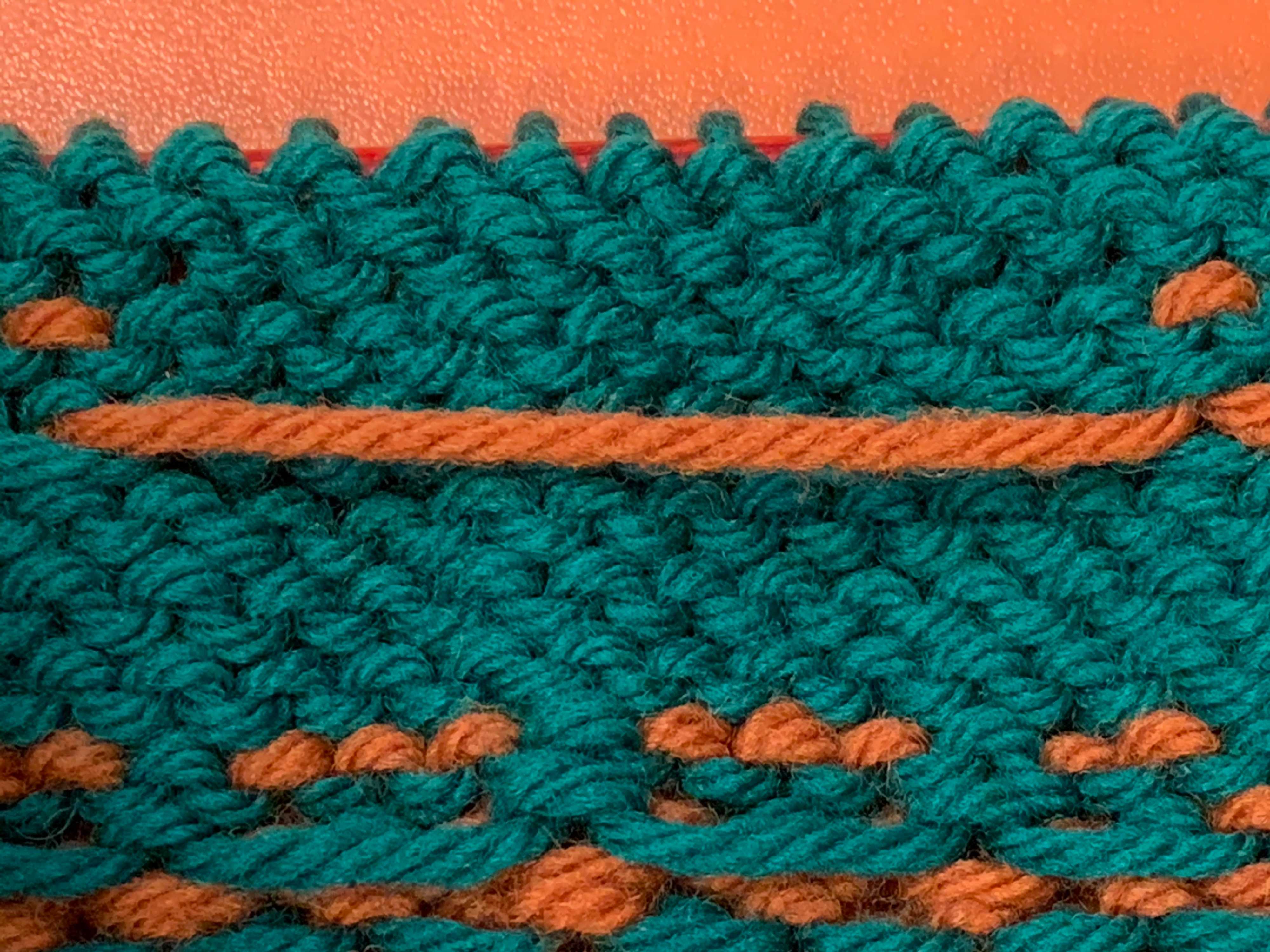 A long float of orange yarn which has not been secured.